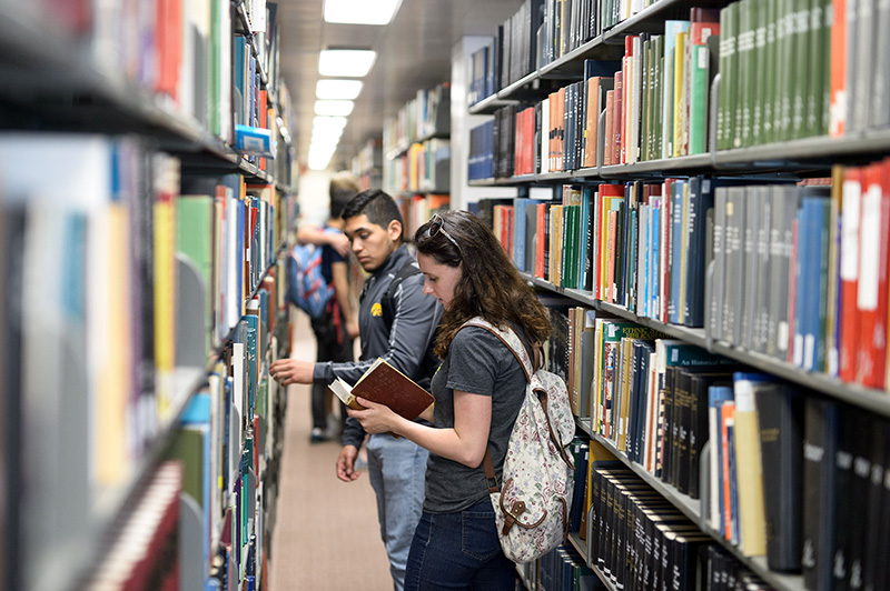 Students in the library looking at shelves of books