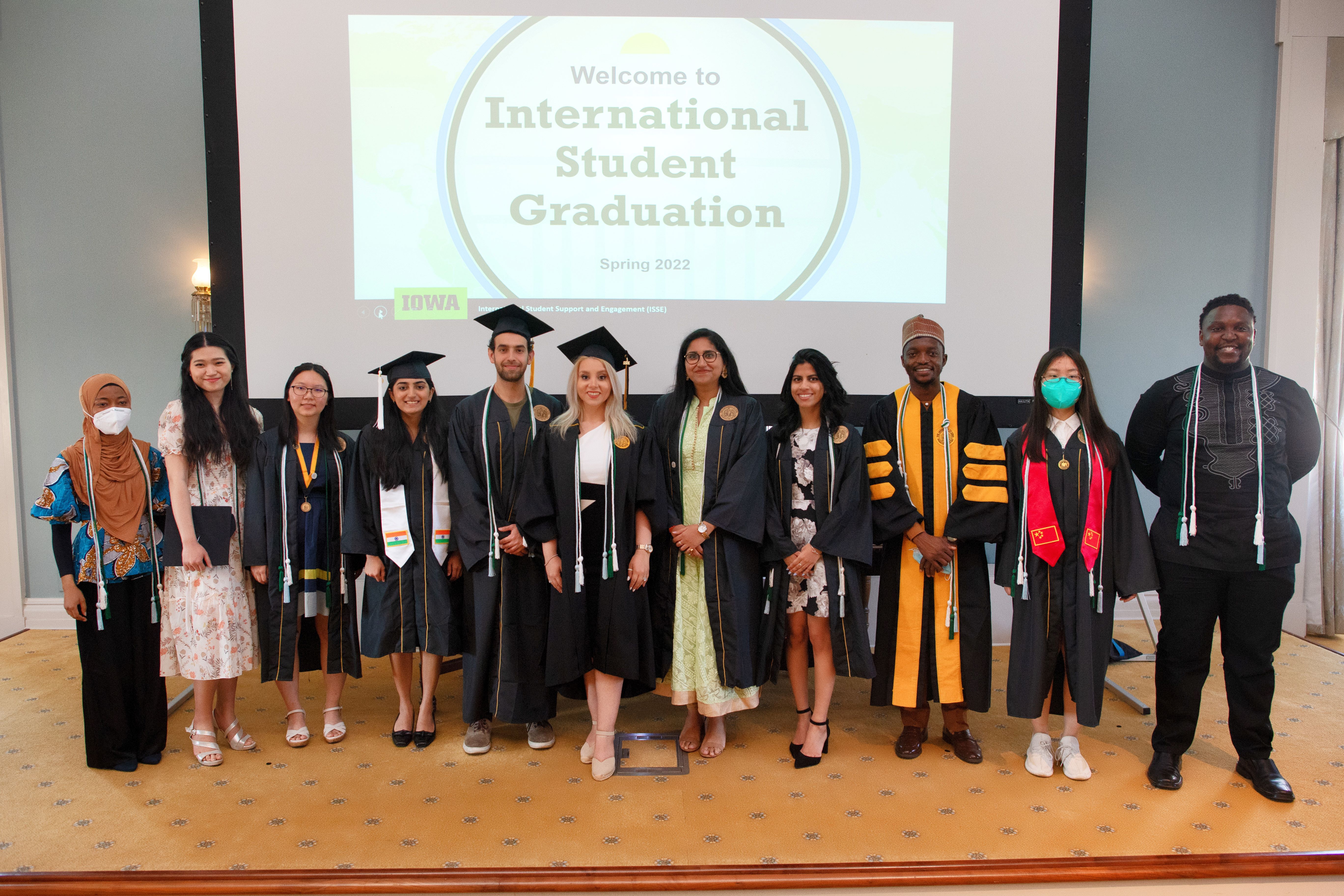 a group of international students wearing the international student graduation cord standing in front of a screen says "welcome to international student graduation" 