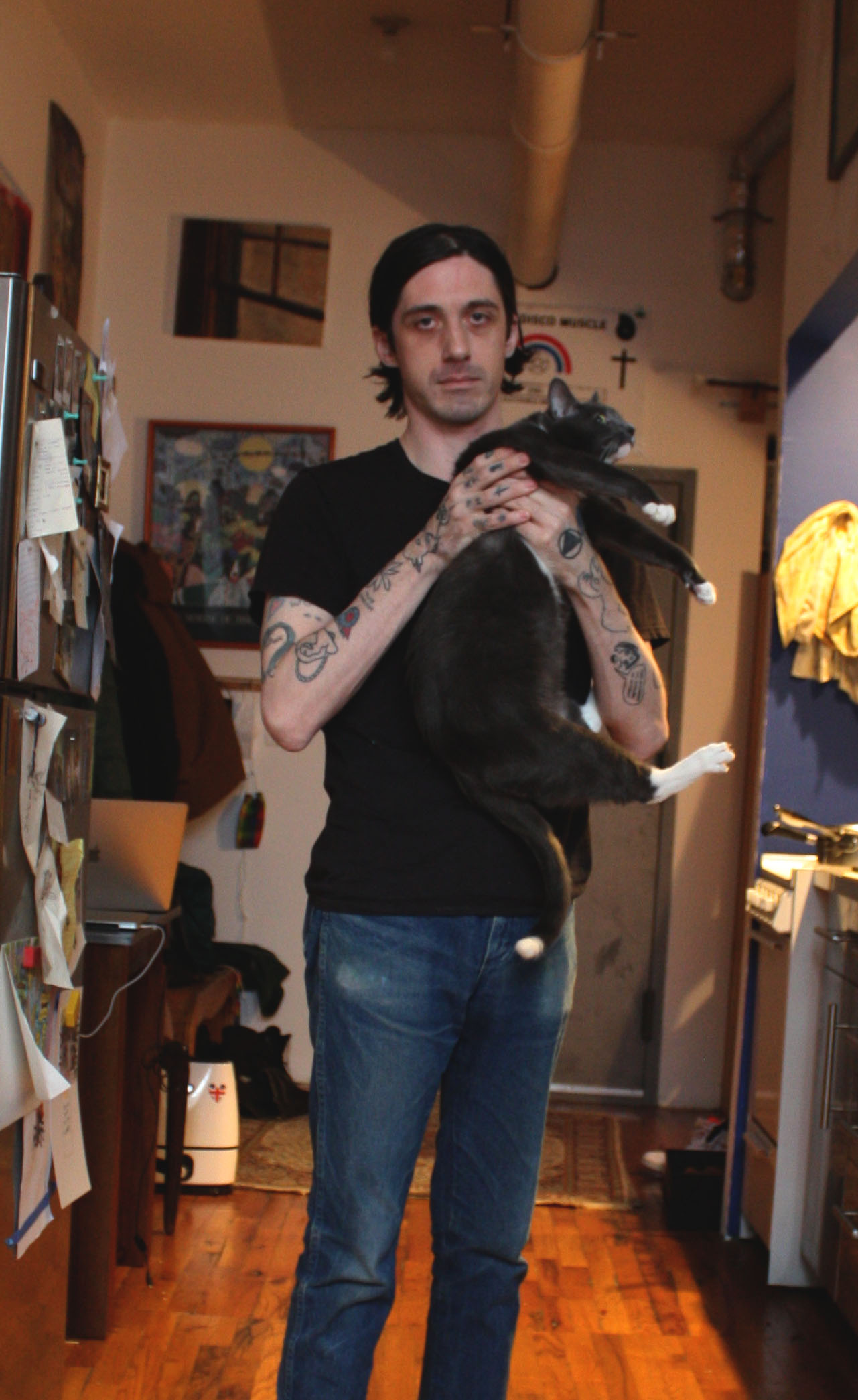 Abe Lampert holding cat standing in room with wood floor