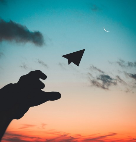 Hand throwing paper airplane into the sky at dusk