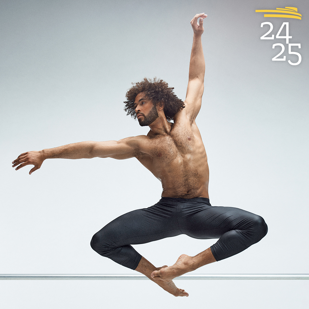 Alvin Ailey male dancer in leaping pose with toes pointed together and knees out with left arm above his head and right arm following his eyes to the right