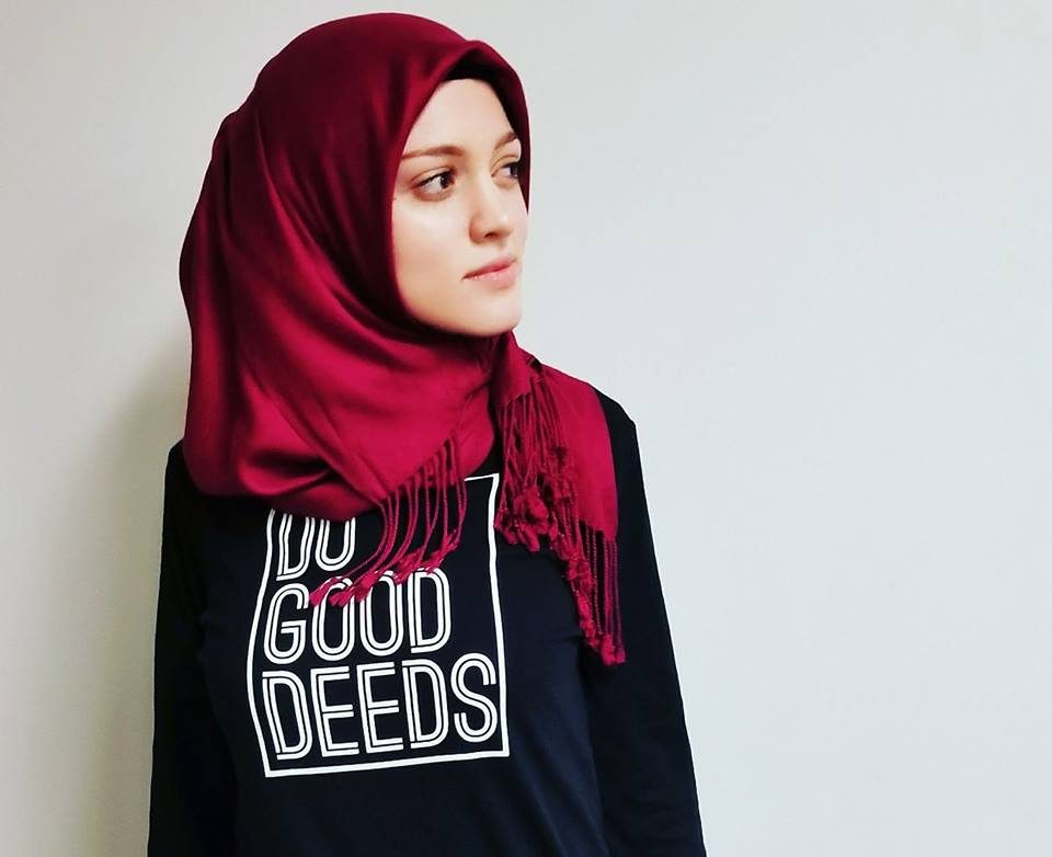 Amal Kassir, wearing a bright red head scarf and a black tee shirt that says "do good deeds"
