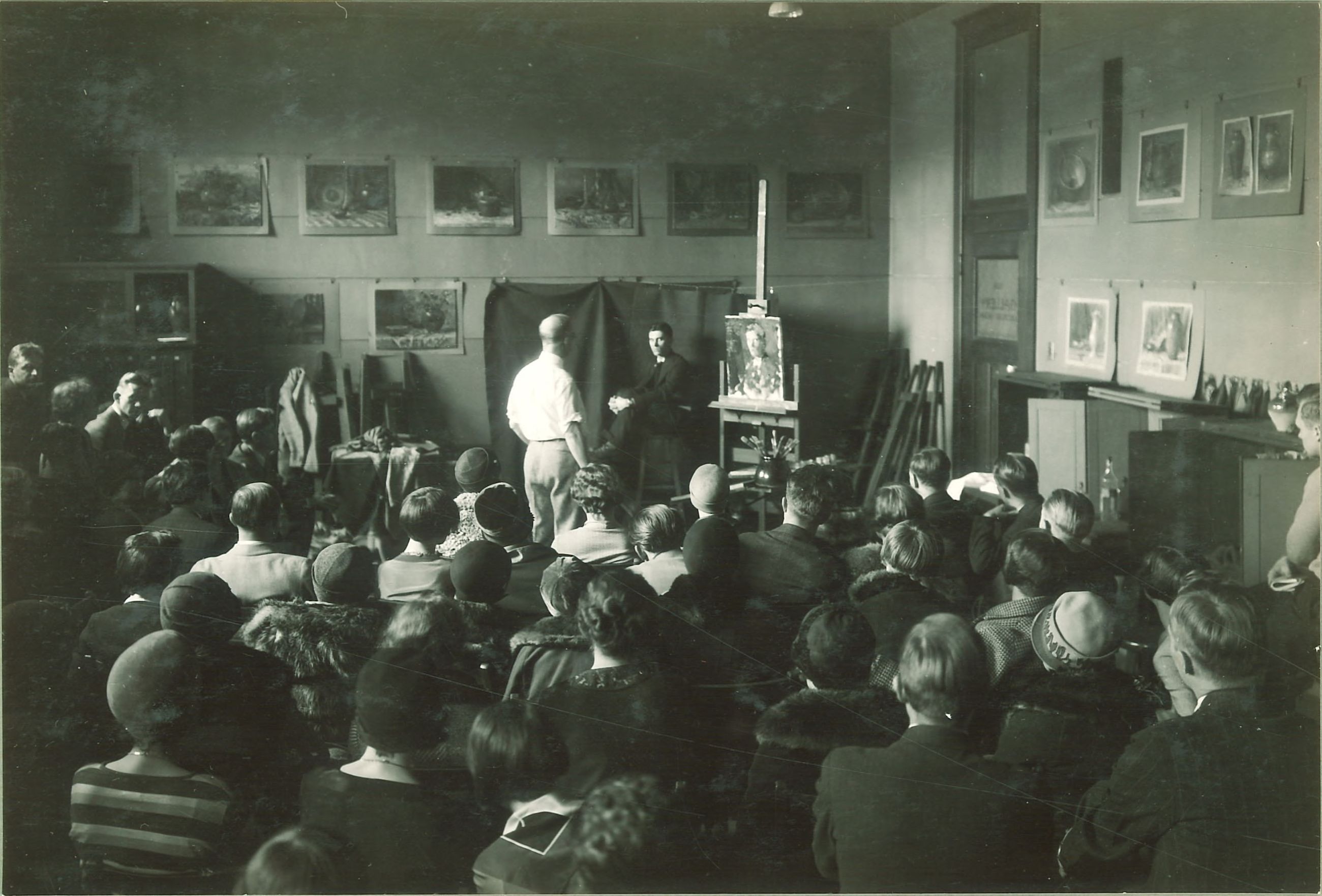A photograph of a full classroom watching a man paint a portrait of a live model at the University of Iowa.