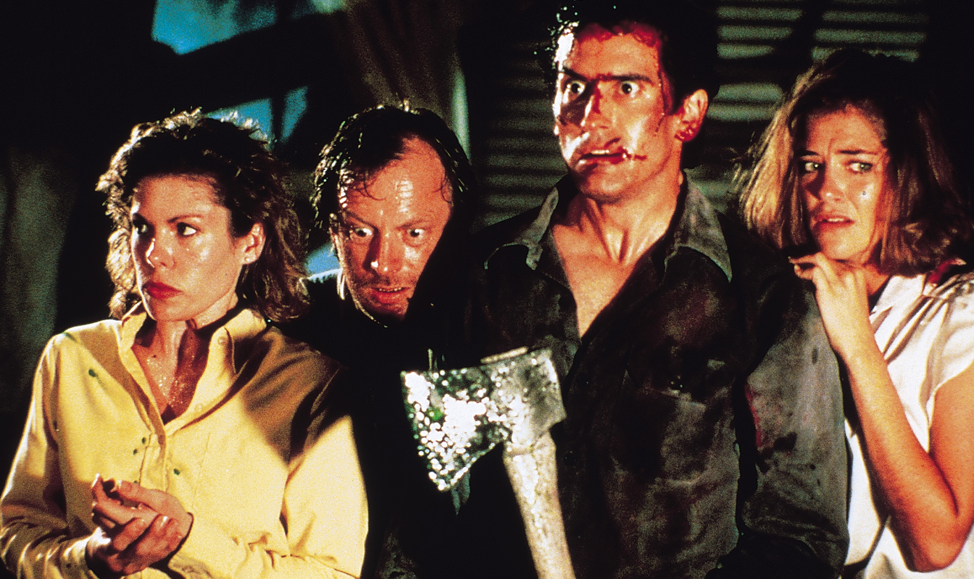 A still from Evil Dead 2. Four characters stand close to each other in fear of approaching zombies.