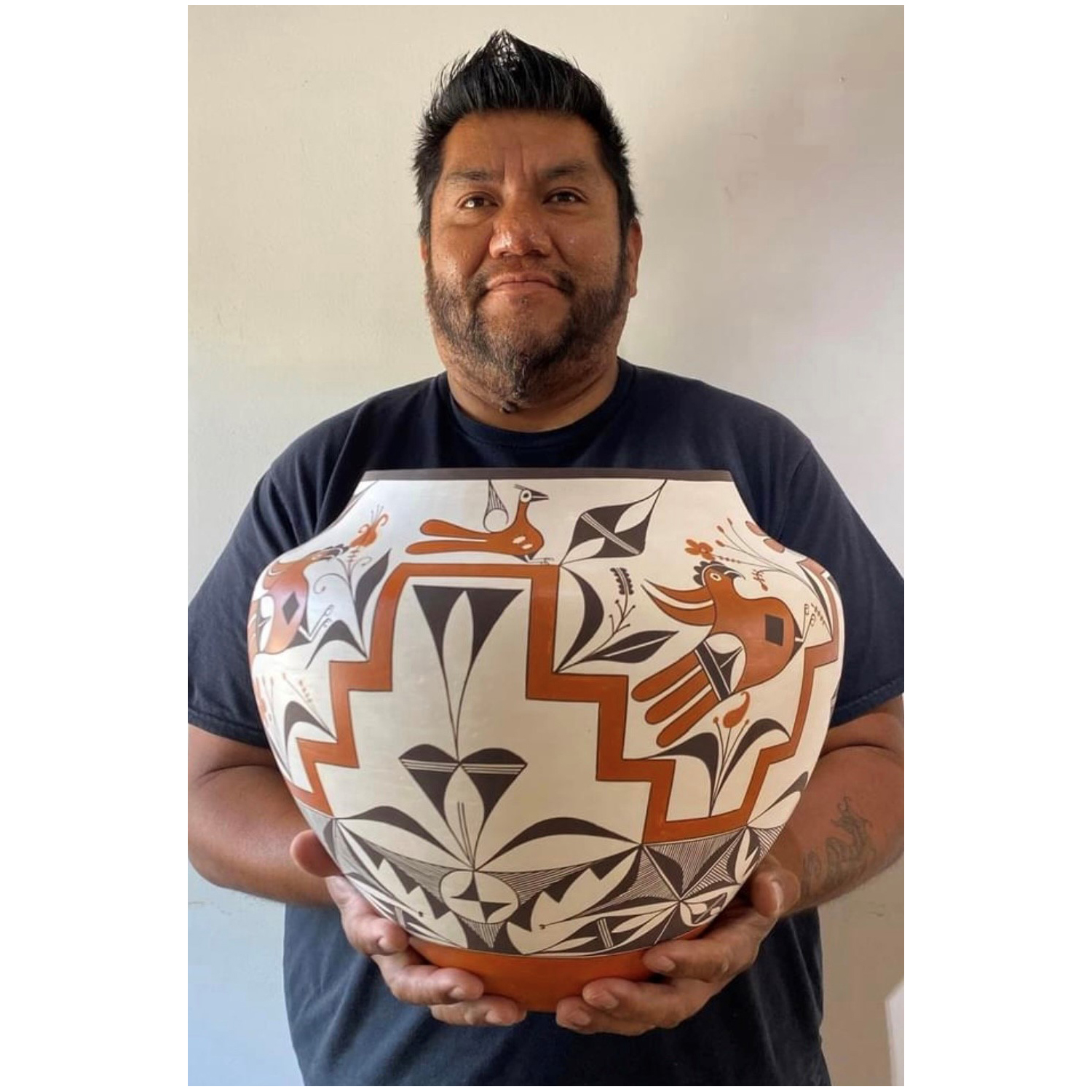 Man with short, dark hair holding a large, round, ceramic pot with geometric designs