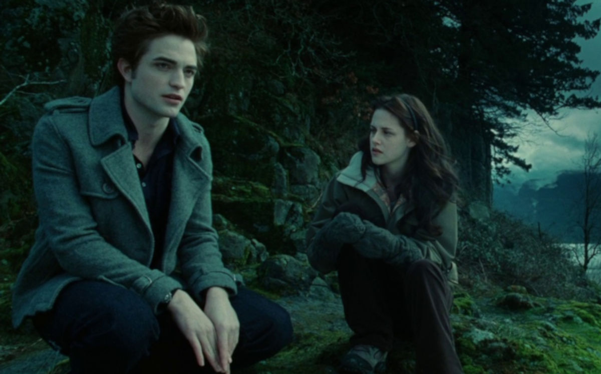 A teenage boy and girl sit together in a dark forest.
