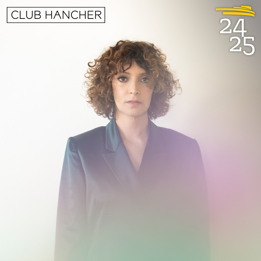 Gaby Moreno standing facing the camera in a blue suit. Club Hancher text treatment in upper left corner