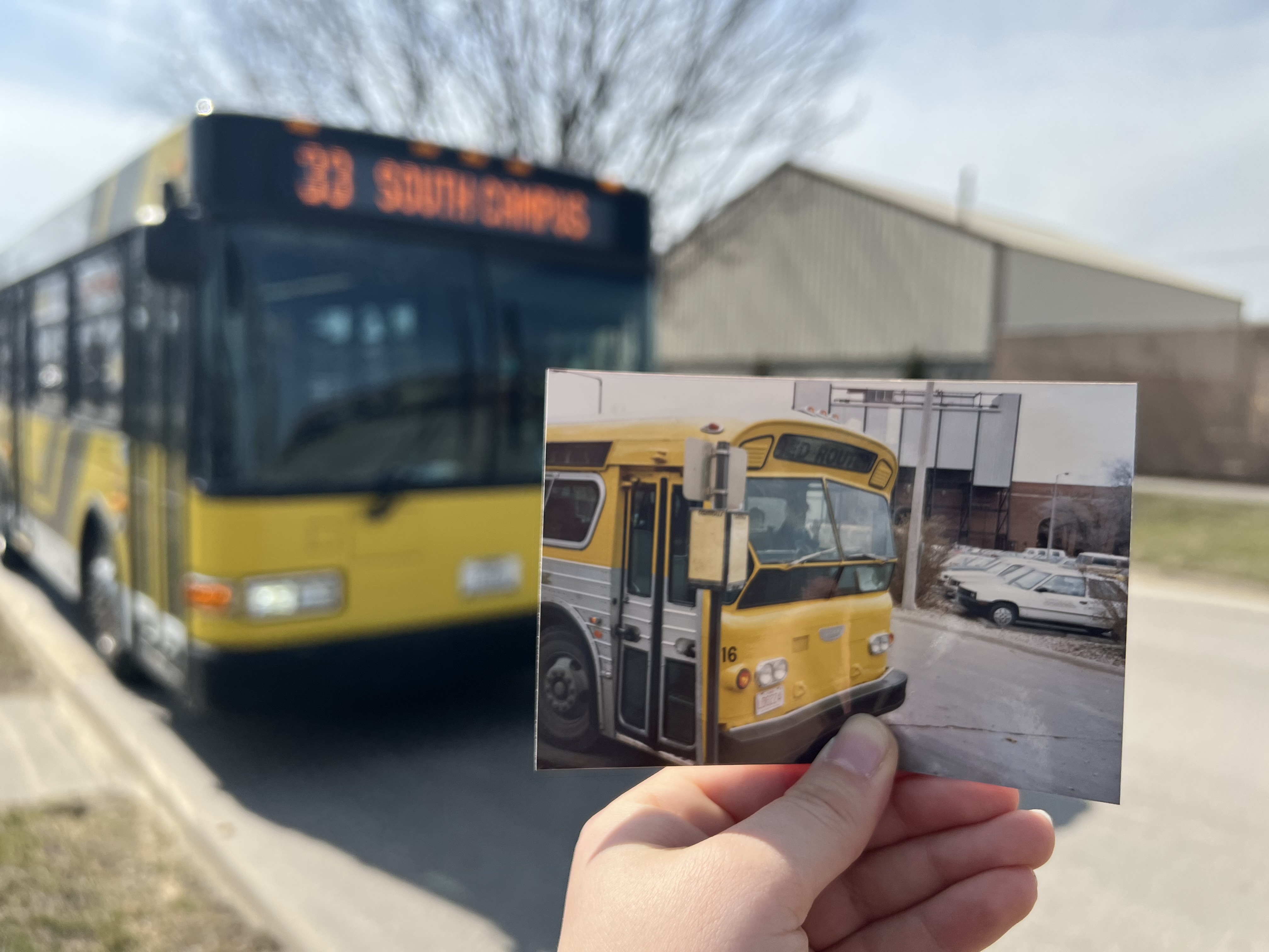 A photo of a 1977 bus is held up in front of a CAMBUS in 2022