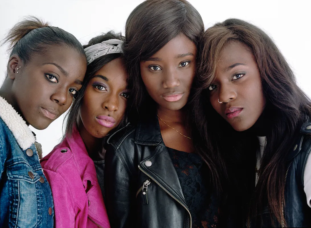 Four teenage Black girls in denim and leather stand in front of a white background.