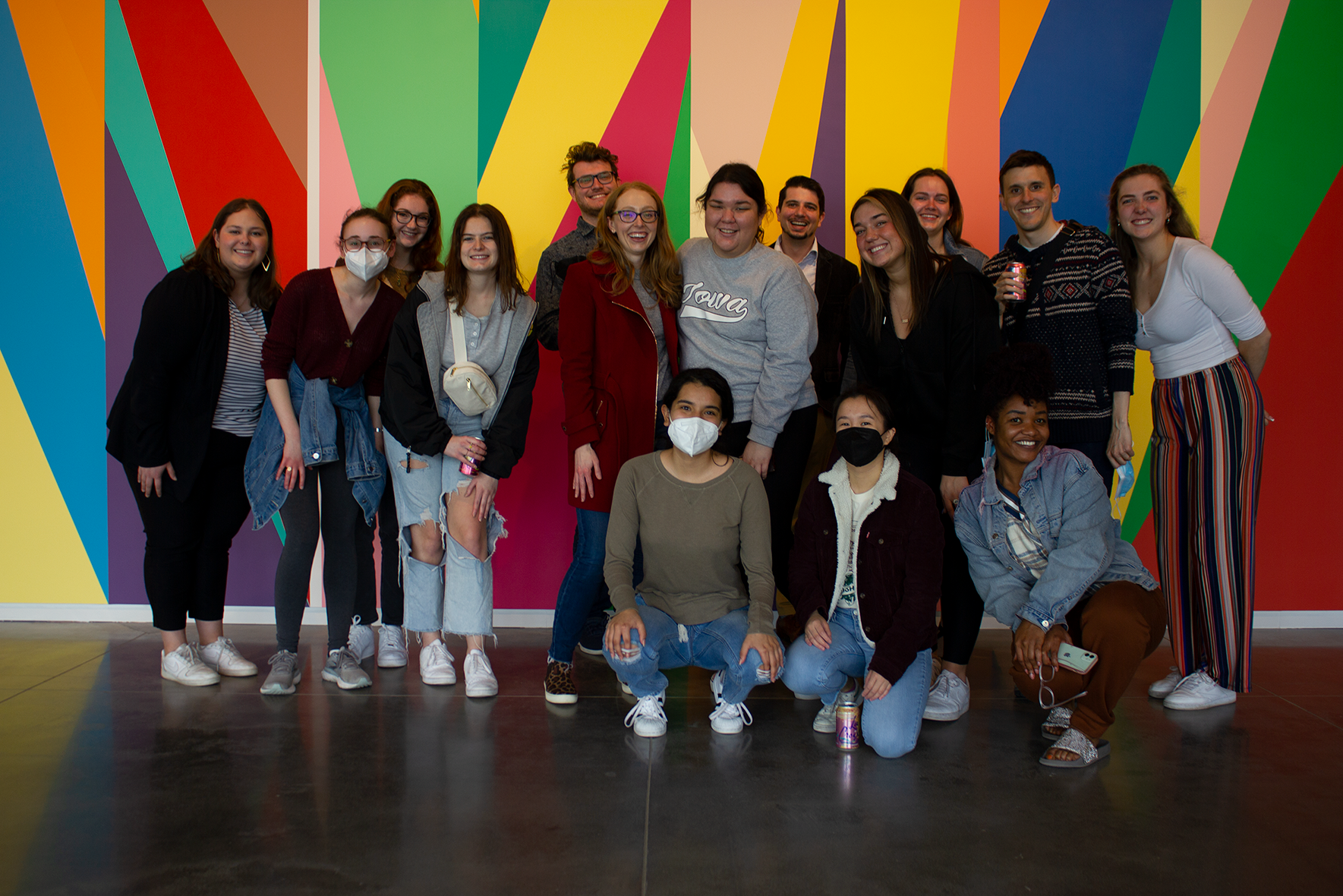 A group photo of students in the Stanley Museum of Art lobby, standing in front of a colorful mural by artist Odili Donald Odita.