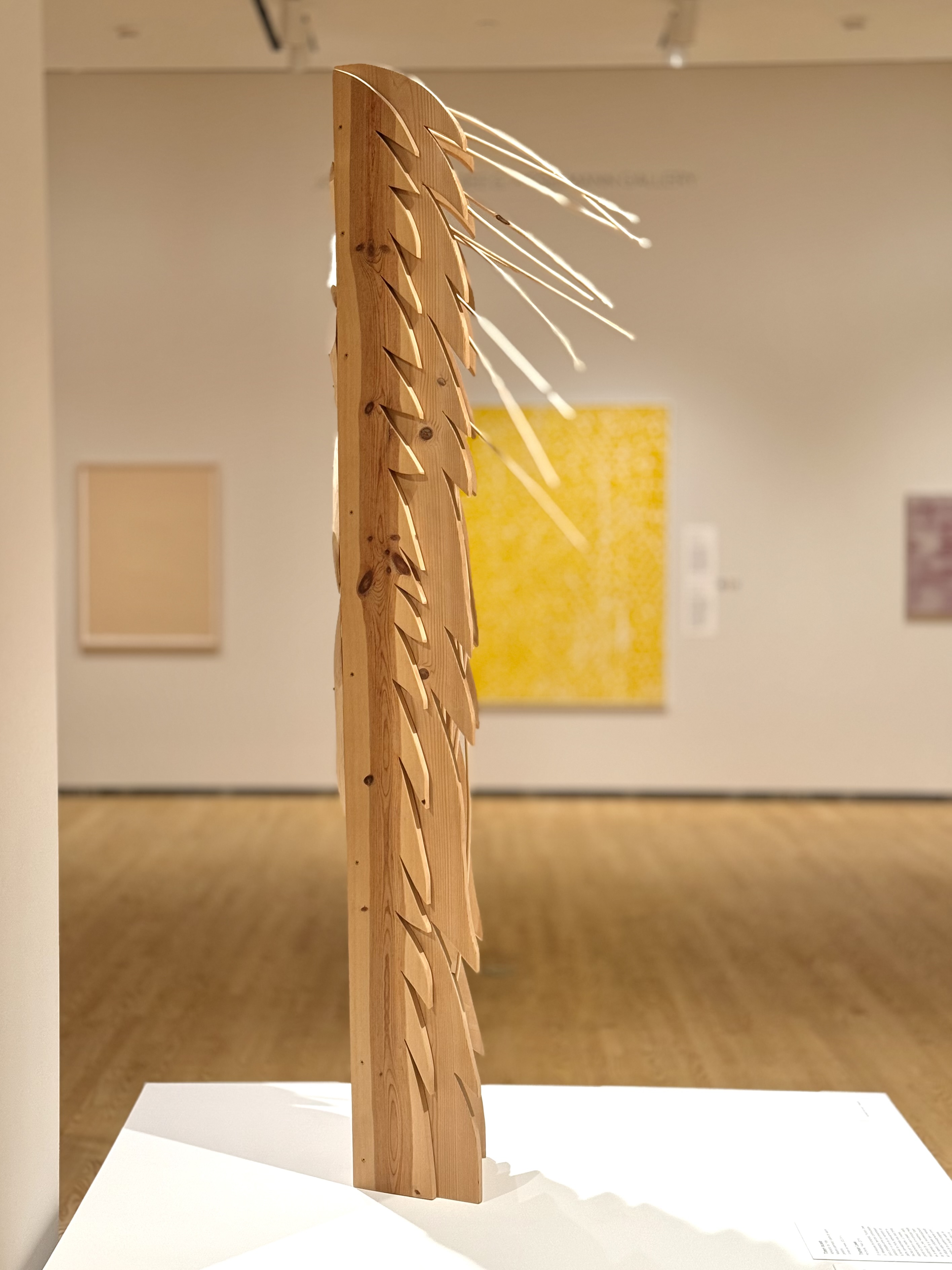 A vertical wooden totem structure standing on a white platform in a gallery