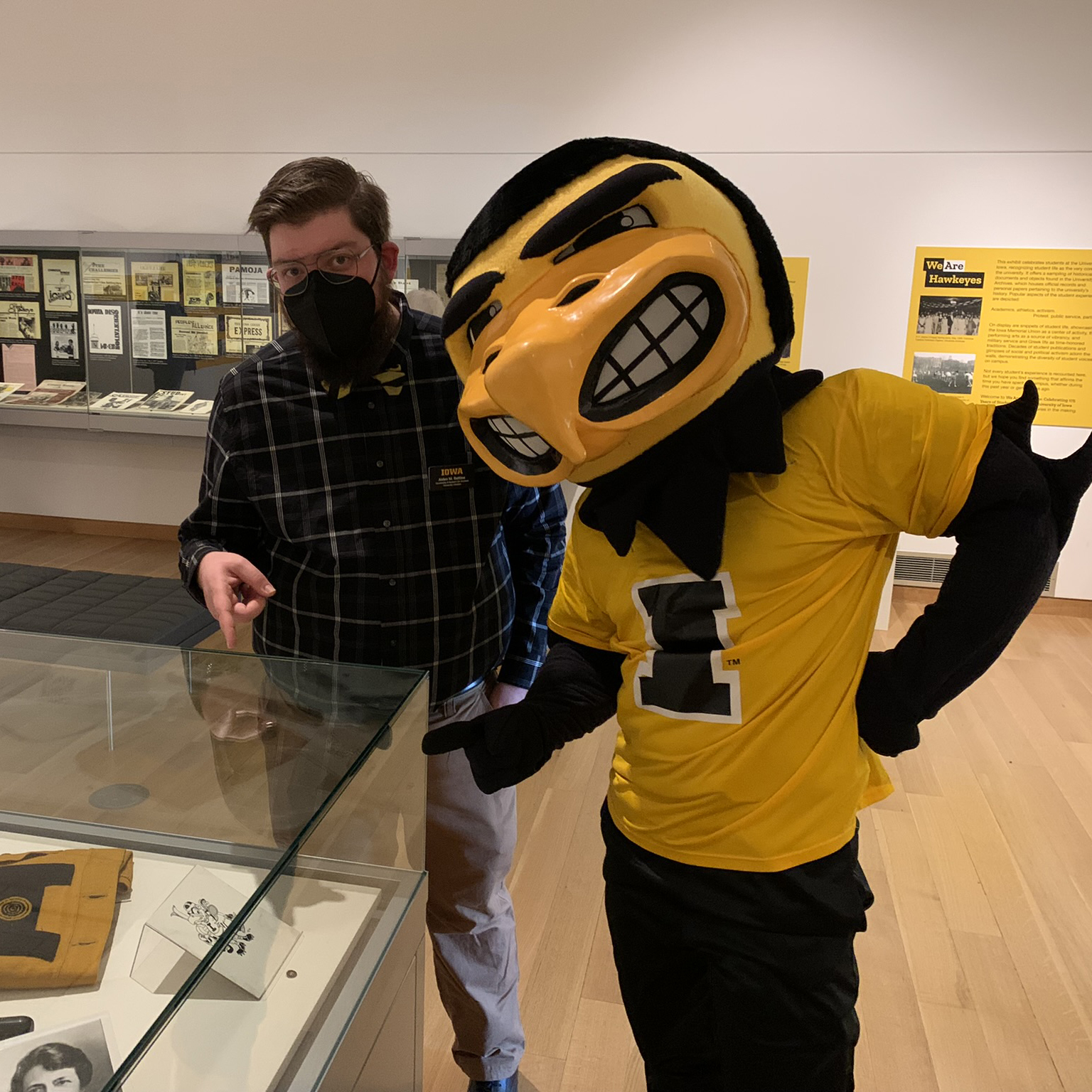 Aiden and Herky stand next to a display case and point at an original Herky drawing by Dick Spencer.