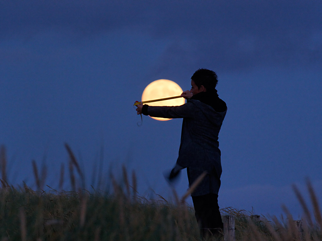 Photo of person trying to measure moon with tape measure