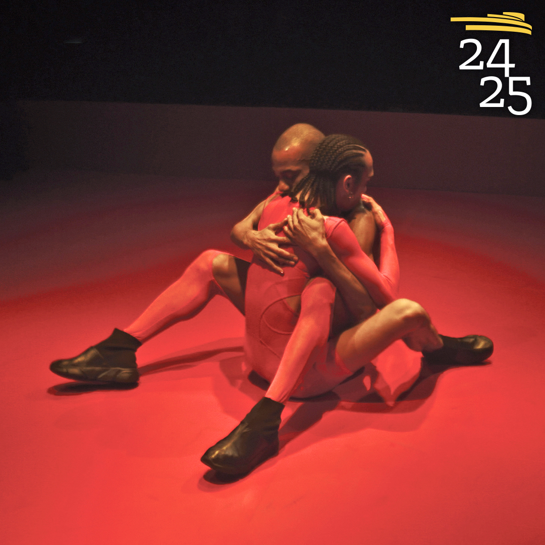 two dancers in red body suits embracing against a red floor