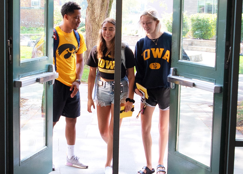 Three Iowa students walking into a campus building. 