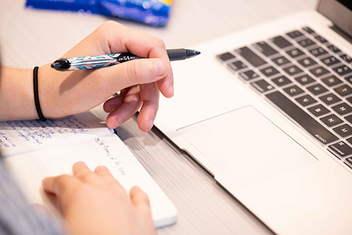 Close up of a student taking notes from a computer.