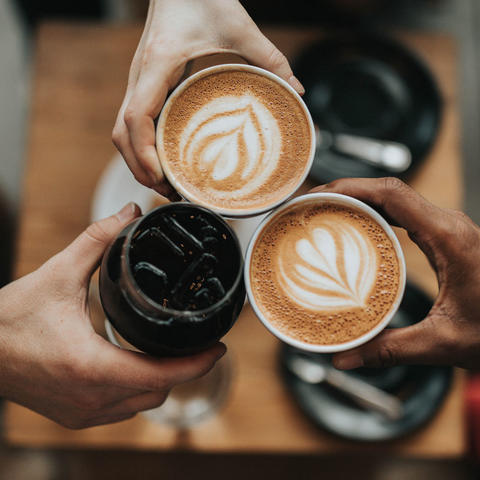 three hands toasting cups of coffee
