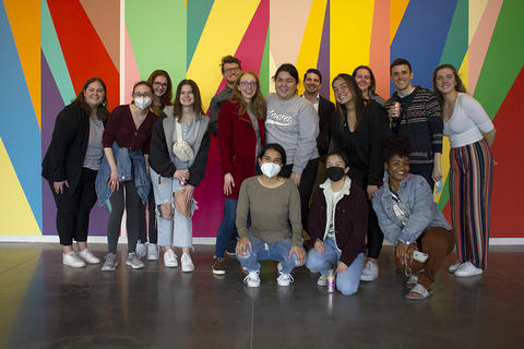 A group of students pose in front of a brightly painted wall mural