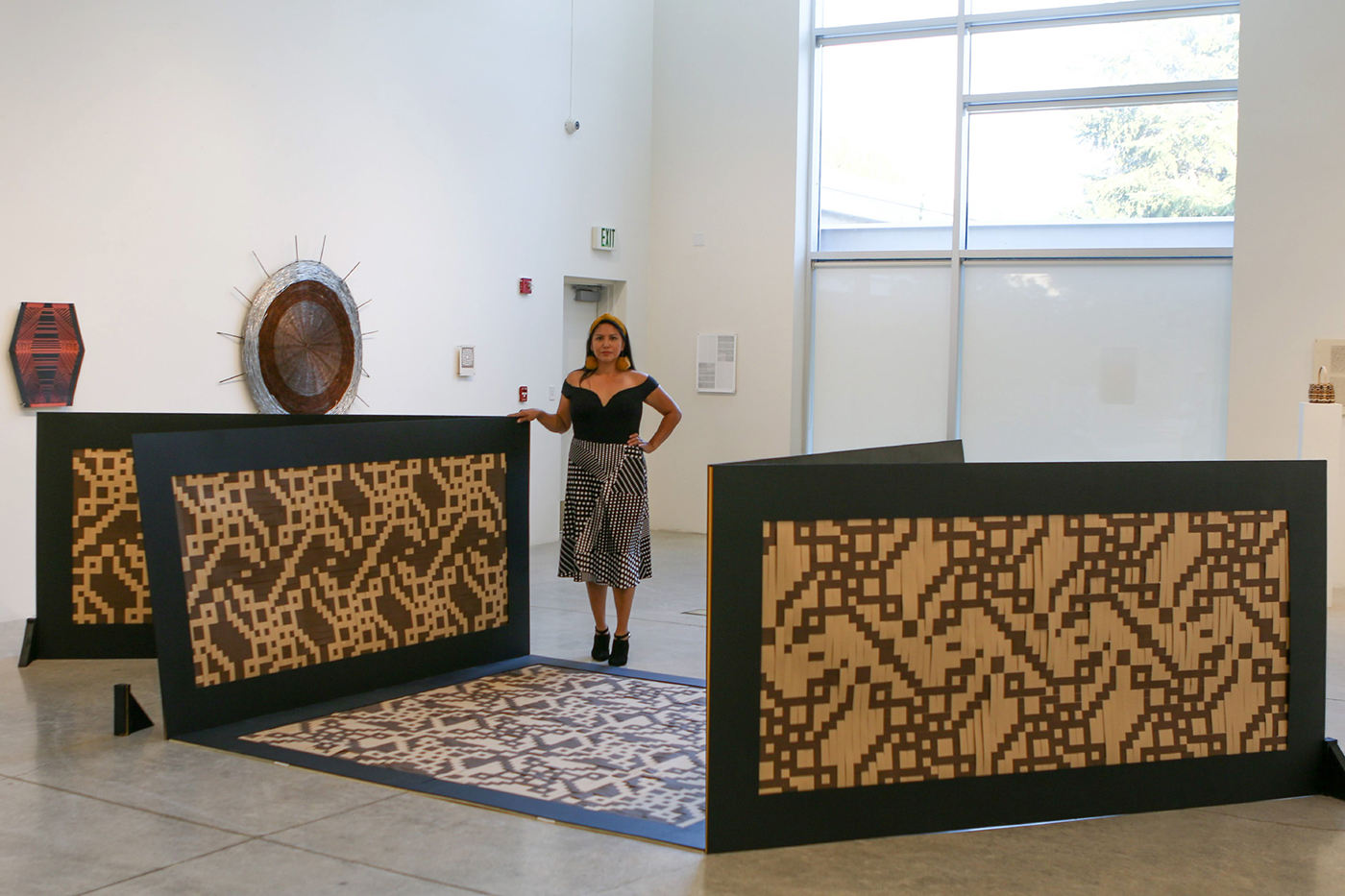 Artist Skye Tafoya standing amidst her large scale work. The work is "life sized" weavings that were attached to boards and stand alone in a gallery space. 