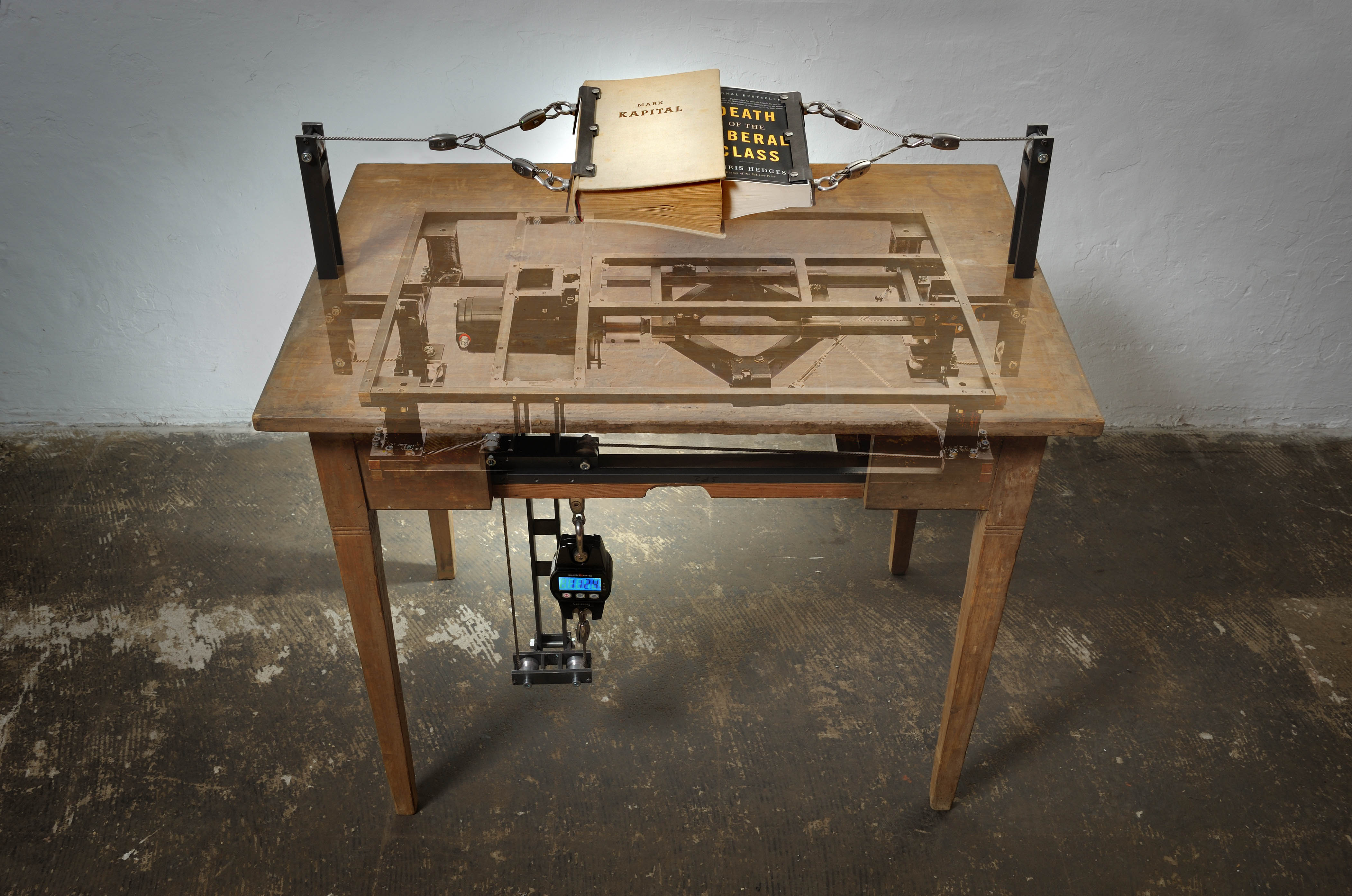 Wood table with book suspended over it held with clamps. mechanism hanging below table