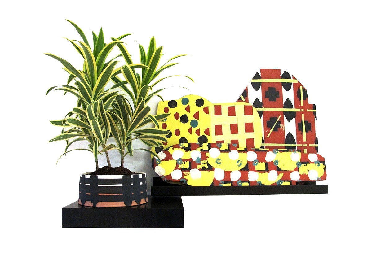 green and yellow leafed plant in dirt in ceramic container with black painted fence on it on a black shelf with a multicolored barn yard ceramic piece on an attached shelf to the right