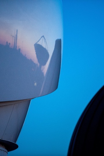 A picture of the dome on top of Van Allen Hall with a reflection of a radar dish and the sunset over the hospital.