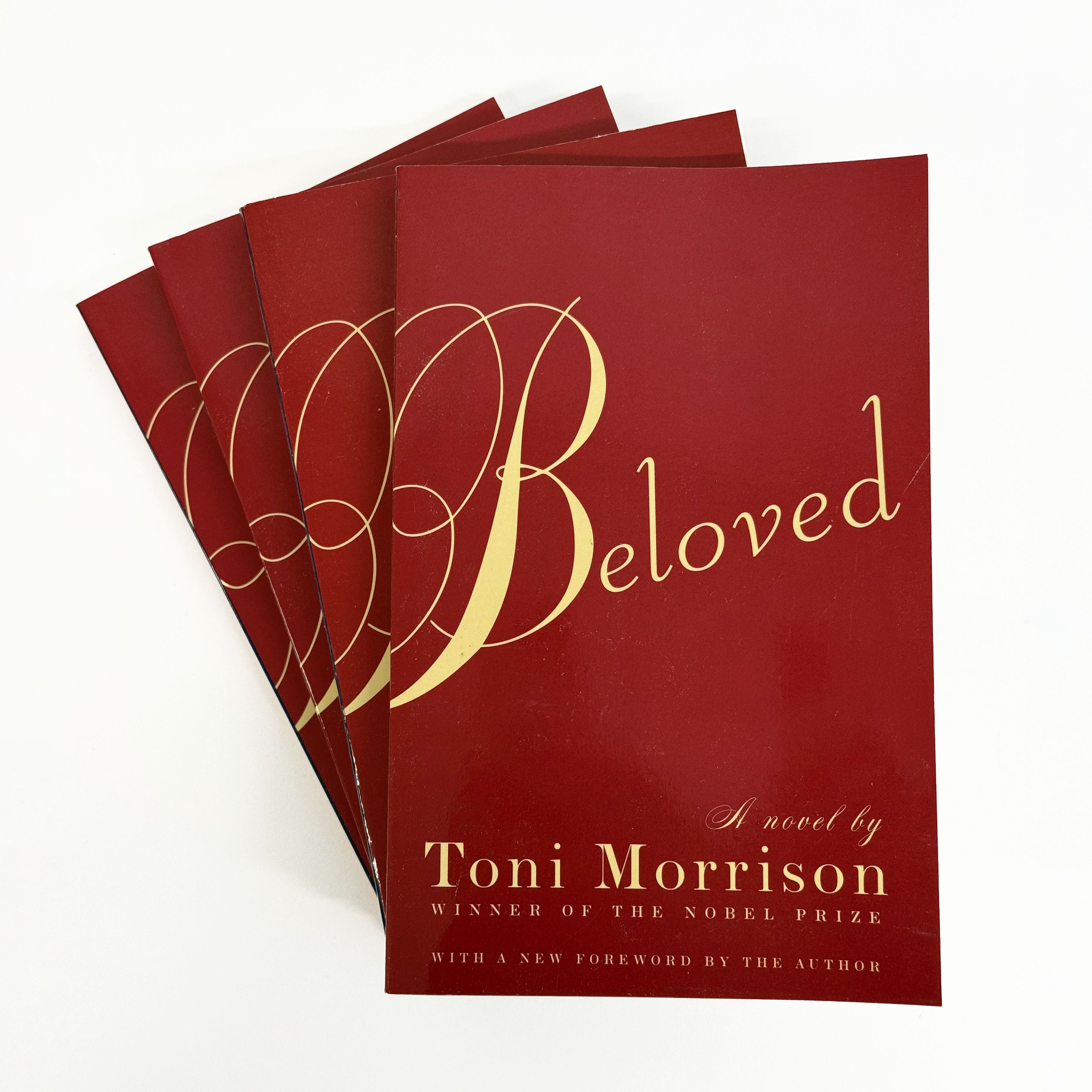 Three copies of a red book fanned out, titled "Beloved. A novel by Toni Morrison" 