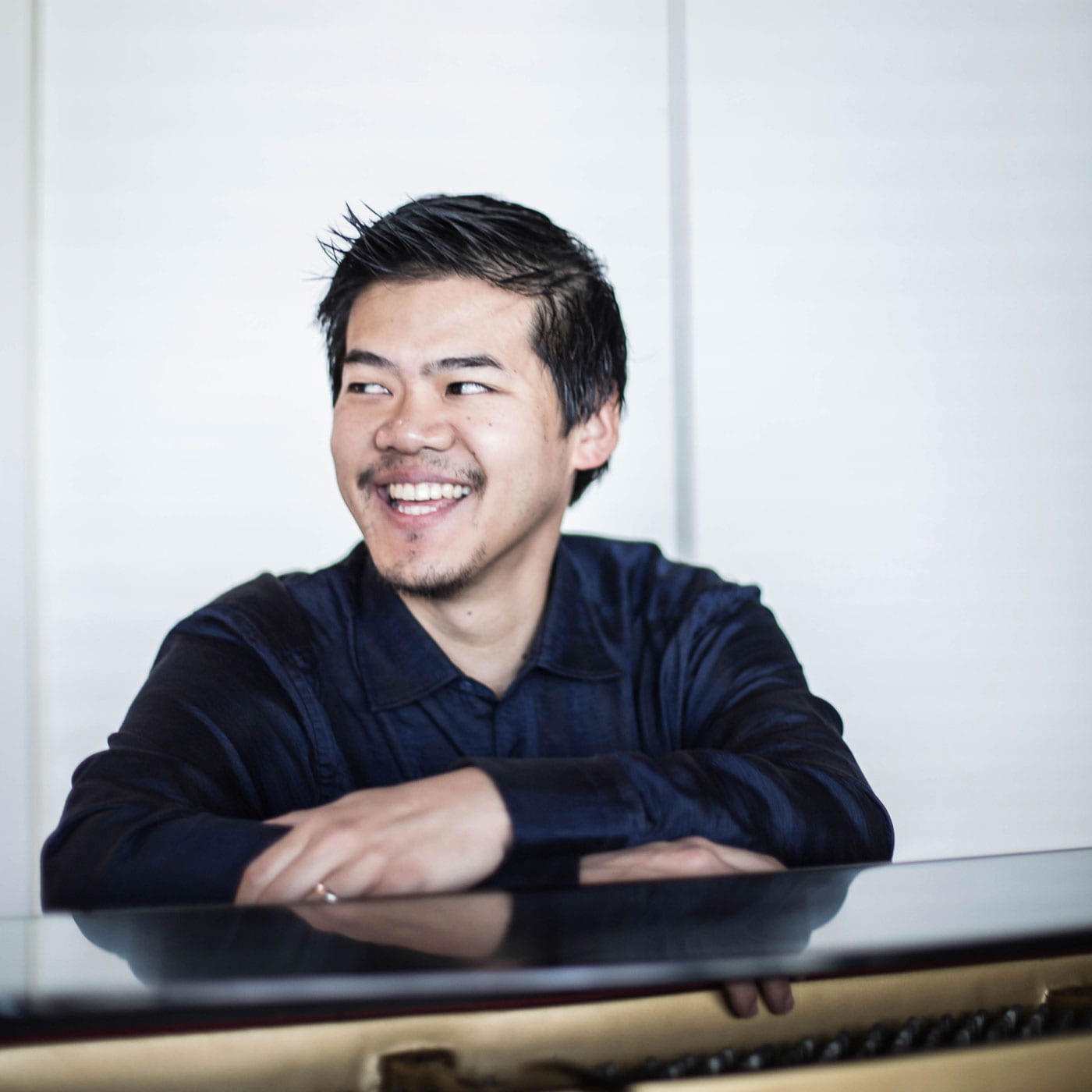 Winston Choi, smiling with his arms crossed atop a piano